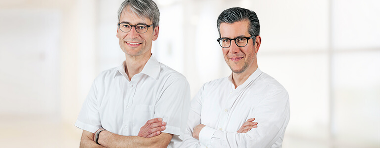 zwei Männer mit weißen Oberteilen und schwarzen Brillen 